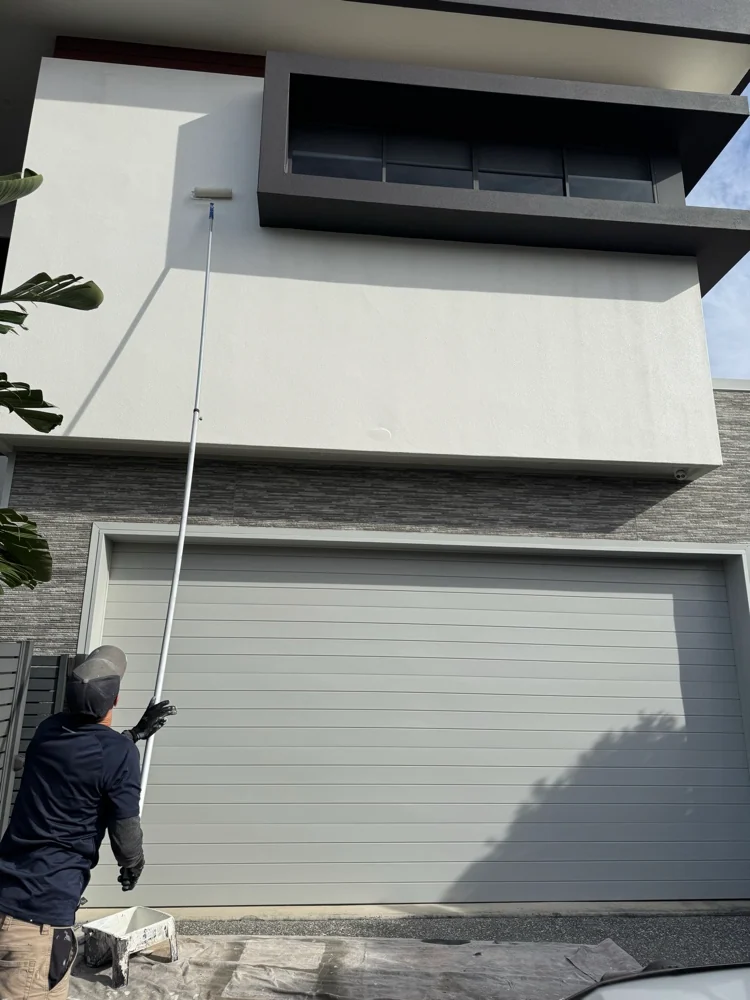 Painter working on the white exterior of a two-storey house