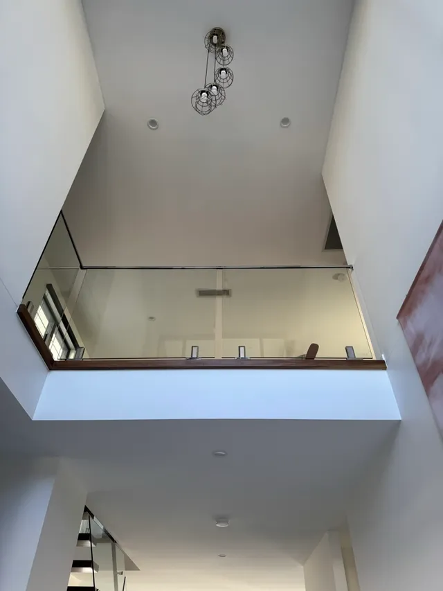 White walls and high ceiling surrounding a glass-balustrade mezzanine and pendant lights