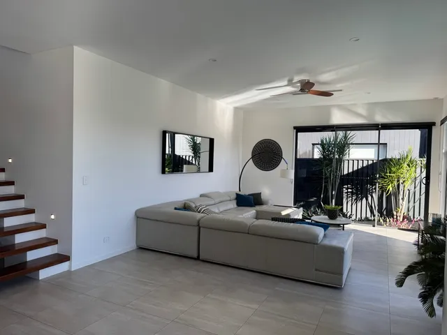 White painted living-room walls and ceiling with a grey sofa, timber stairs and black window frames